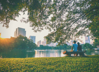 Imagem mostra duas pessoas sentadas em um banco dentro de um parque.