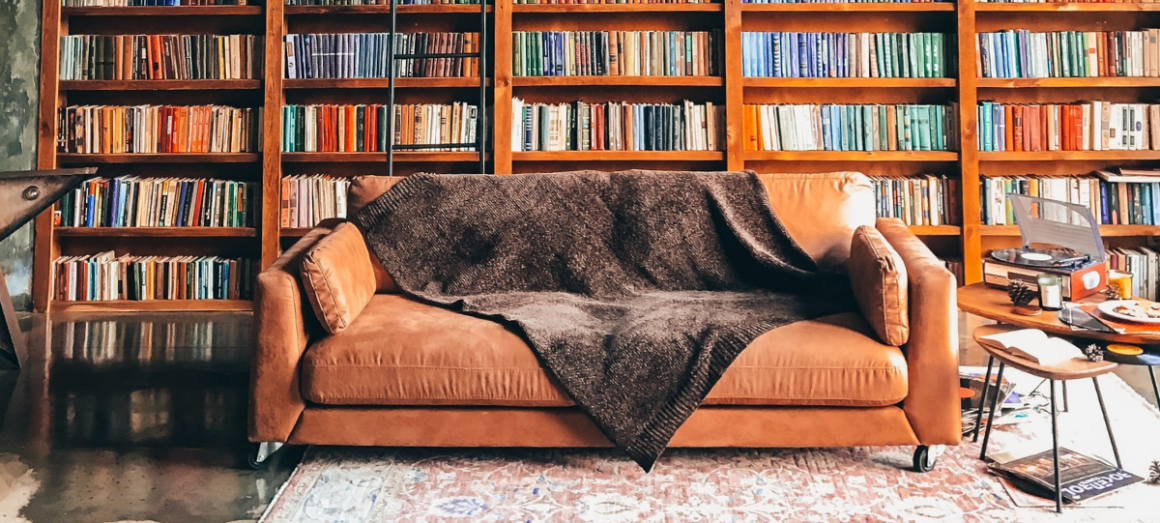 Imagem de um sofá a frente de uma parede com uma estante repleta de livros.