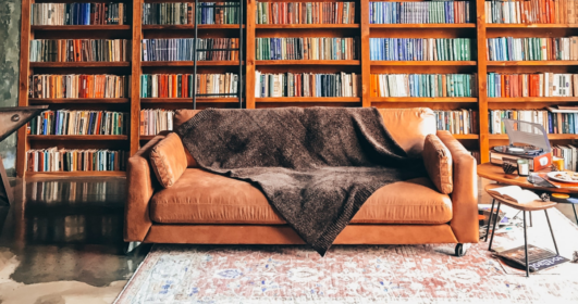 Imagem de um sofá a frente de uma parede com uma estante repleta de livros.