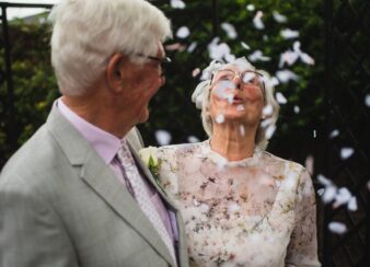 Foto de um casal de idosos se divertindo com pétalas de flores que caem no ar.