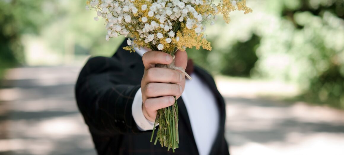 Homem segurando um buquê de flores à frente do rosto.