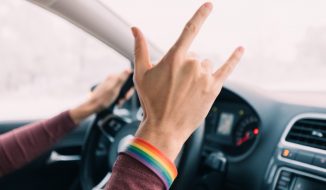 A mão de um motorista de carro fazendo o sinal de rock and roll com um bracelete de arco-íris.