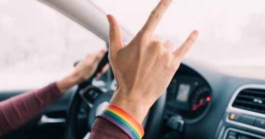 A mão de um motorista de carro fazendo o sinal de rock and roll com um bracelete de arco-íris.