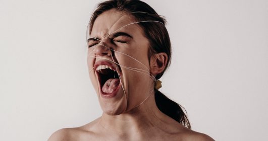 Imagem de uma mulher gritando com um fio enrolado no rosto e no cabelo.