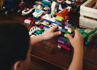 Criança brincando com peças coloridas de lego em uma mesa. Cinco perfis sobre neurodiversidade que você precisa acompanhar.
