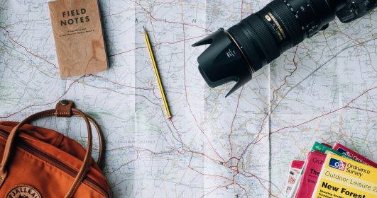 um grande mapa com uma bolsa, câmera, livros e um caderno de anotações. Slow travel.