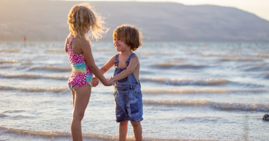Imagem mostra duas crianças de mãos dadas na praia.