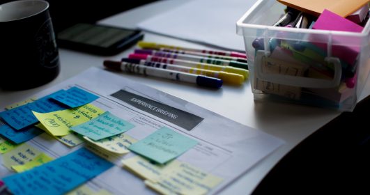 imagem de papeis, post-it, canetas e uma calculadora em cima de uma mesa.
