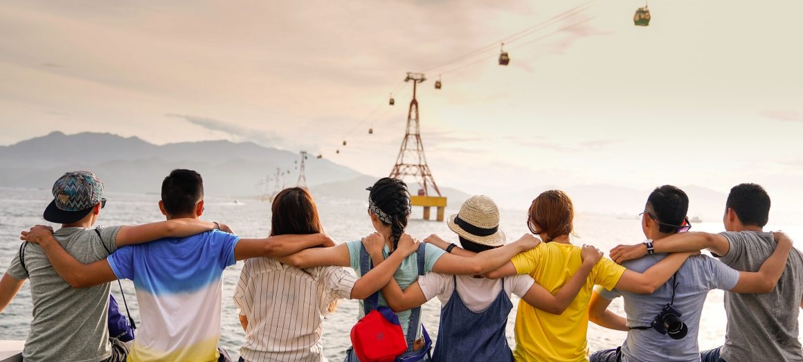 Pessoas abraçadas em um píer apreciam a vista para o mar enquanto estão unidas pelos braços. Como começar a praticar a solidariedade.