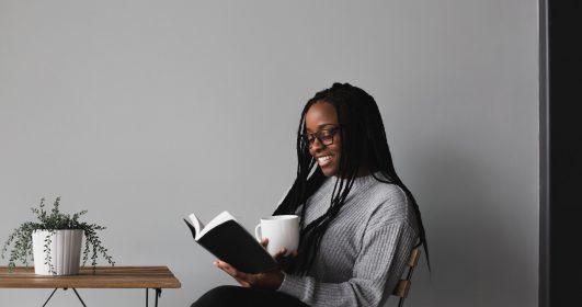 Imagem de uma mulher lendo um livro e segurando uma xícara.