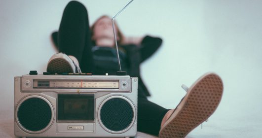 Imagem de um rádio antigo e uma pessoa deitada ouvindo música.
