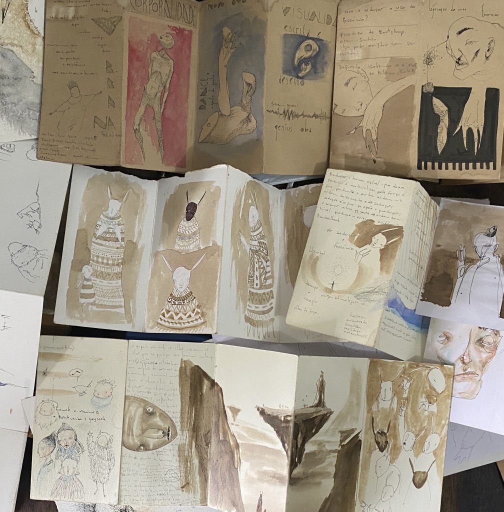 foto de vários sketch books sanfonados em uma mesa com desenhos diferentes. Arte