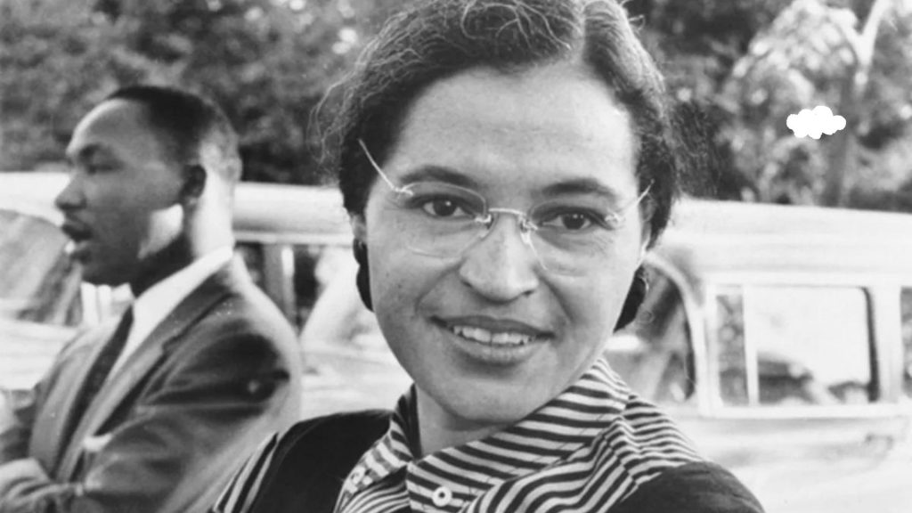 Rosa Parks usa óculos de grau, cabelo preto e sorriso discreto. A foto está em preto e branco. introvertido