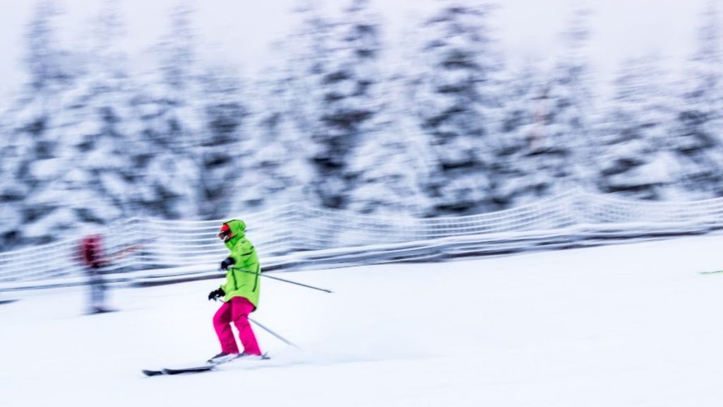 uma pessoa vestindo trajes rosa e verde esquia na neve. 