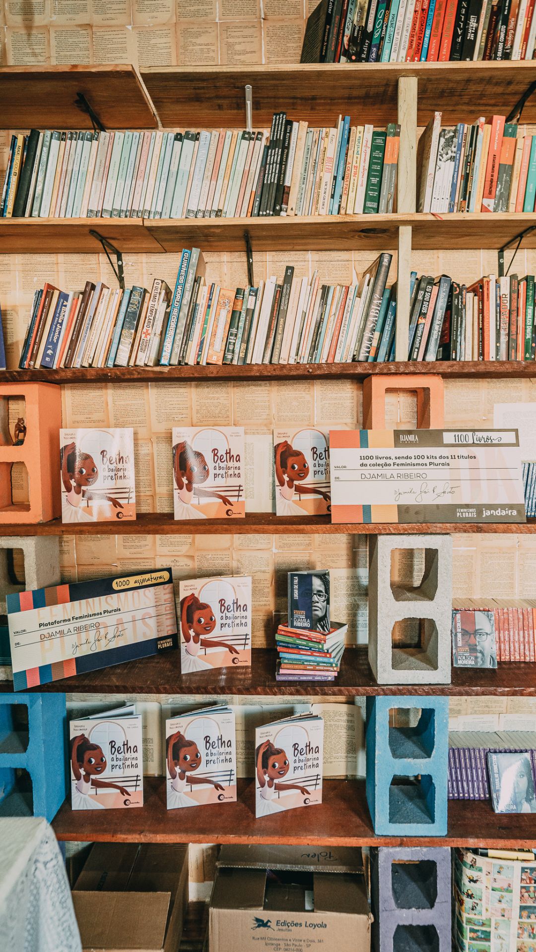 foto de uma estante de livros com diversos livros no local e tijolos de decoração. biblioteca