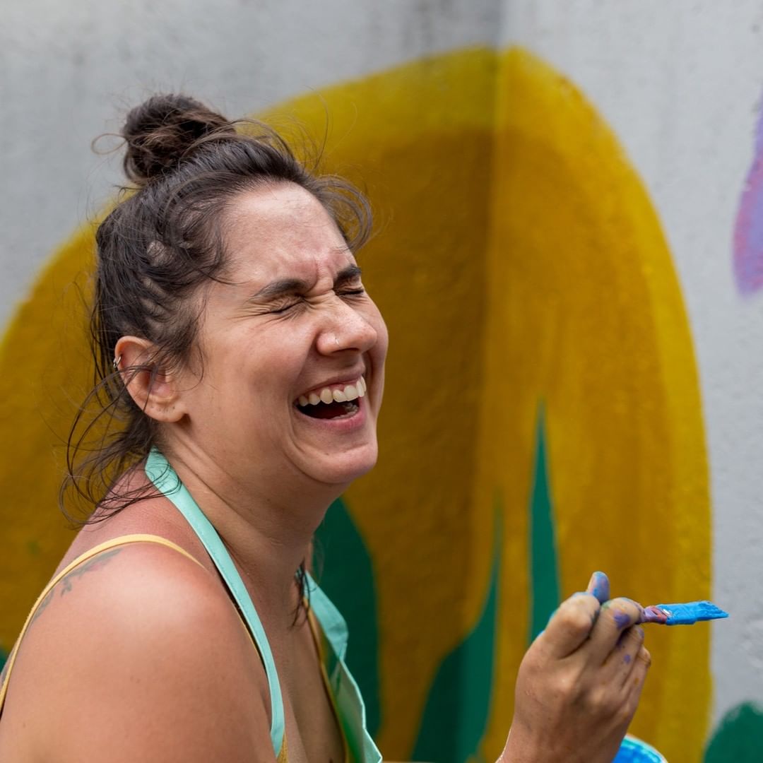 uma mulher sorri pintando uma parede com pincel na mão. arteterapia