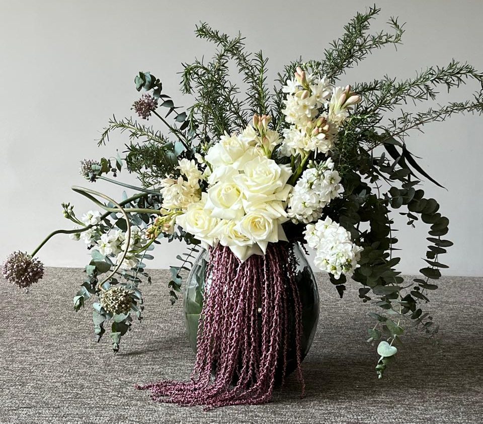 Arranjo com flores e plantas medicinais em uma mesa cinza. 