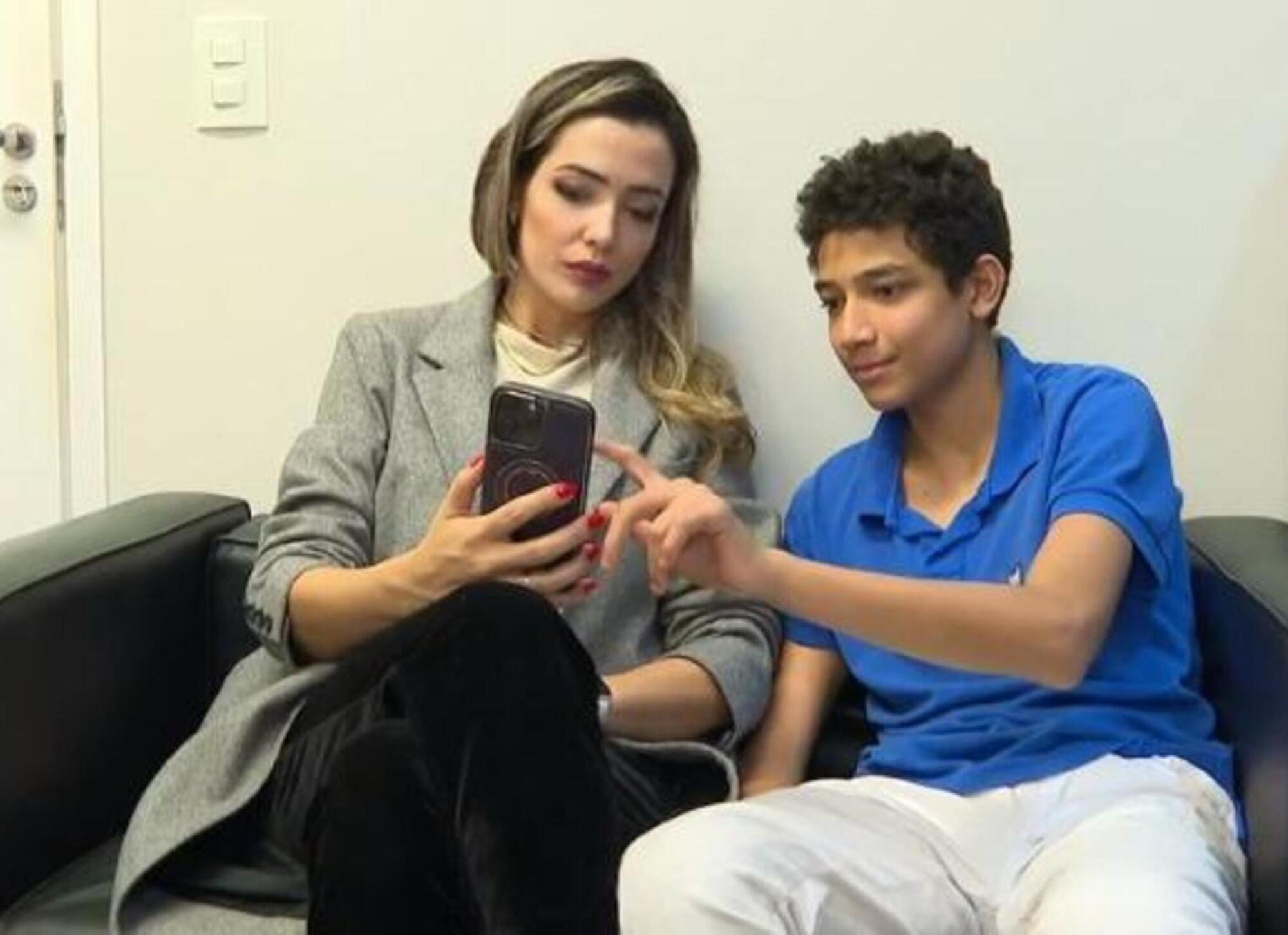 A psicóloga Tatiane e seu filho, Pedro, sentados um ao lado do outro mexendo juntos em um celular